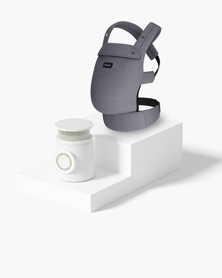 Momcozy Baby Carrier Bundle including a gray baby carrier and a white baby bottle warmer placed on a stepped white platform