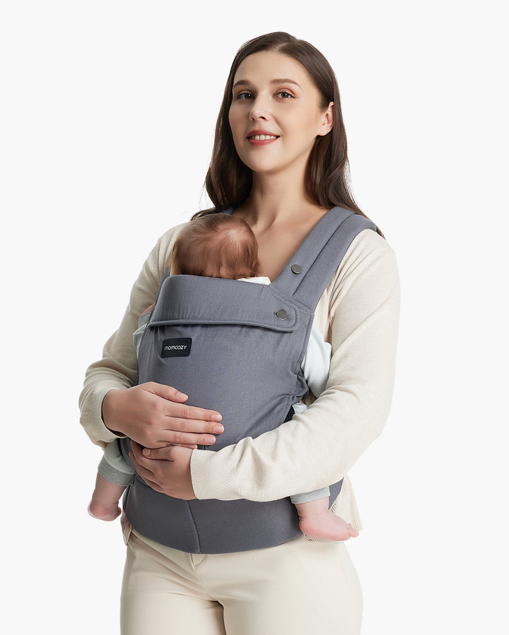Woman carrying baby in a grey Momcozy baby carrier designed for newborn to toddler, showcasing comfortable padded shoulder straps and supportive structure.