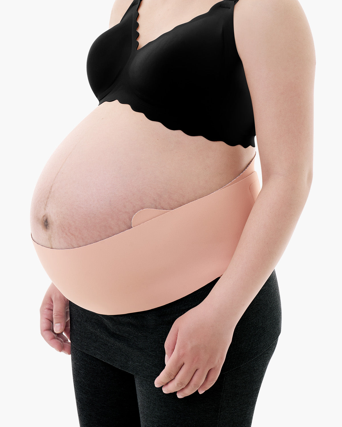 Light beige Momcozy Maternova belly band shown on a pregnant model wearing a black bra and grey leggings.