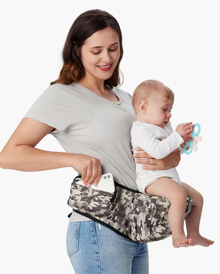 Mother using a camouflage-patterned 3D Belly Protector and EVA Massage Board Baby Hip Seat Carrier, with her baby holding a teething toy. The hip seat carrier has a pocket where the mother is placing a smartphone.