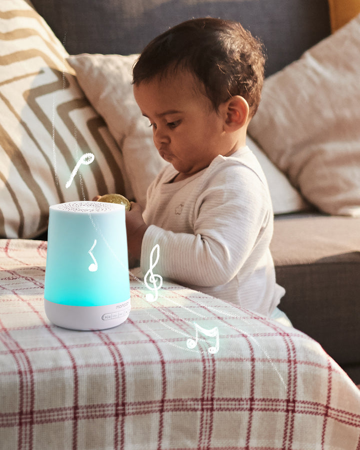 Baby engaged with glowing smart baby sound machine emitting musical notes on plaid-covered table