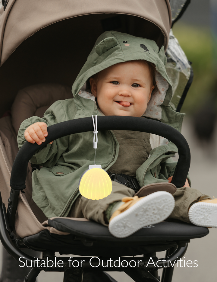 Baby in stroller with Portable Sound Machine, suited for outdoor use, wearing a green coat and sporting a playful smile.