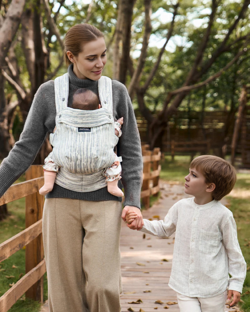 Momcozy PureHug baby carrier in use. Mother babywearing in a striped carrier while walking with her son.