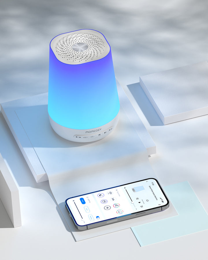 Smart baby sound machine from Momcozy with blue and purple light and app interface on a smartphone for control