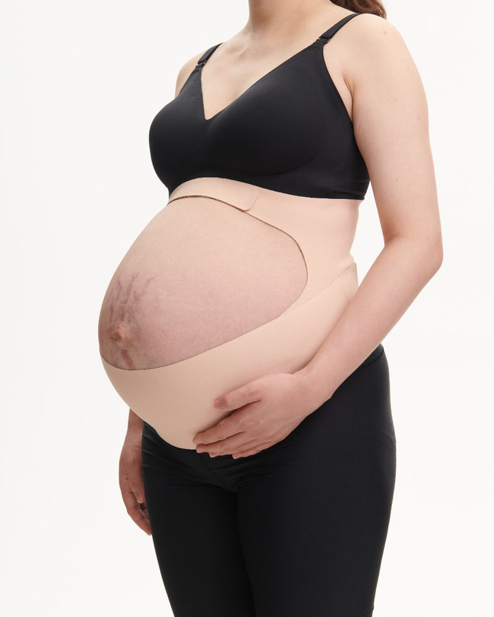 Pregnant woman demonstrates the support provided by wearing an oyster pink Momcozy Ergonest Maternity Belly Band from a side view.