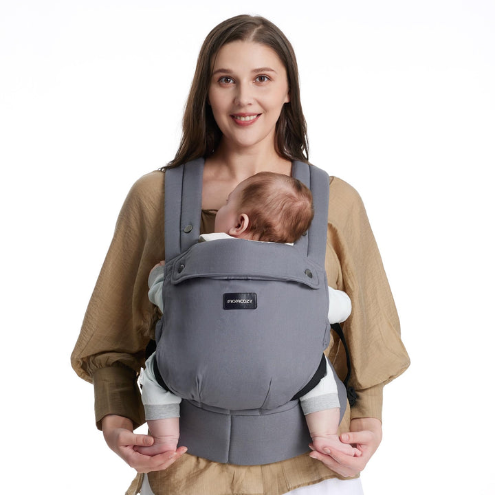 Woman carrying a baby with a grey Momcozy baby carrier for newborn to toddler, illustrating hands-free baby carrying solution.