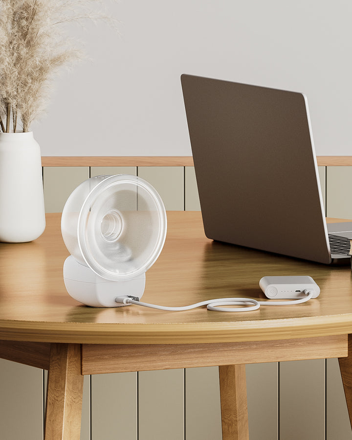 The S9 Pro Wearable Breast Pump, currently charging on a wooden table next to a laptop, offers up to 24 hours of use on a single charge.